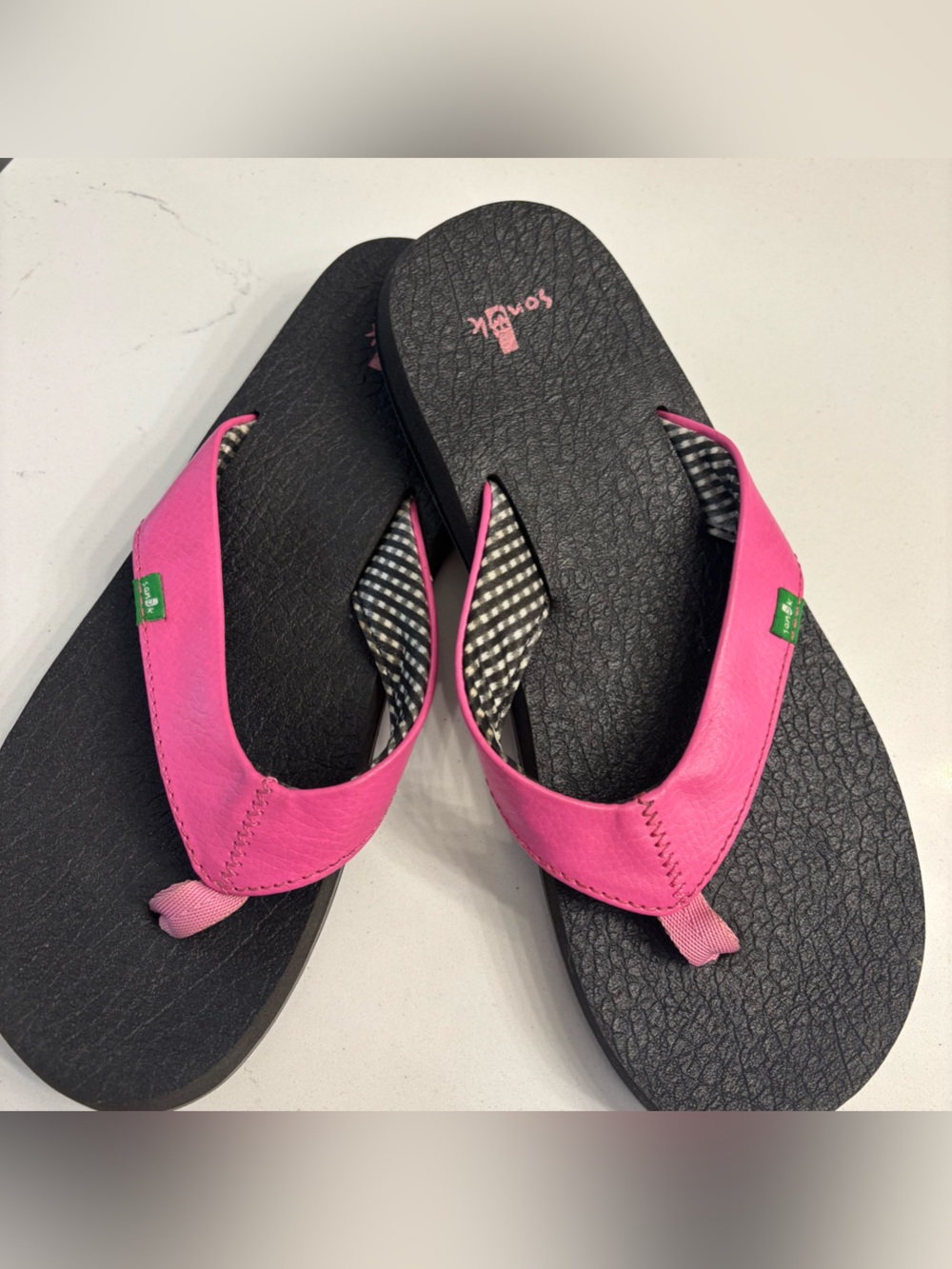 Classic black Sanuk flip flops. Striped fabric on the straps with pink strap.